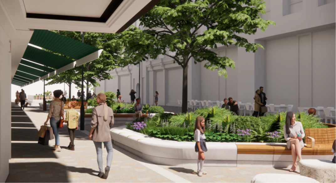 This is an image showing one of the proposed stone planters in detail. A planting scheme is shown with a variety of shrubs, purple flowers and a tree rising centrally. Timber seating is shown on parts of the rim of the stone planter. A proportion of the seating is provided with backrests and armrests. Pedestrians can be seen walking along the street between a line of planters, positioned centrally in the street, and Harrods’ building. Harrods’ green awnings can be seen extending towards but not over the planters. 