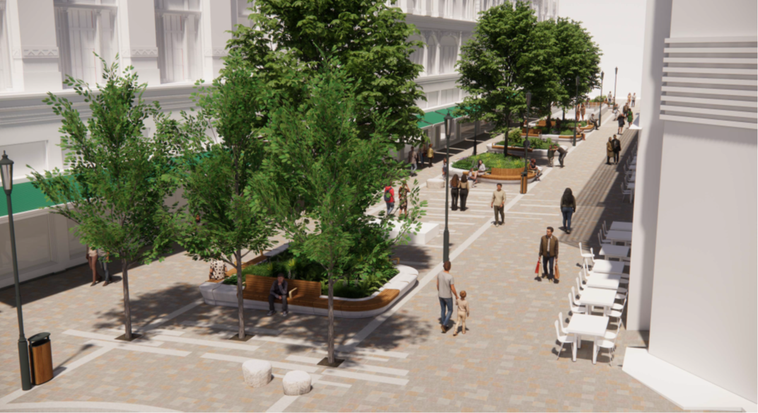 This is an image looking down Hans Crescent from Basil Street towards Brompton Road. It shows six large planters with trees and shrubs positioned centrally along the length of the street. There is timber seating on the rims of the stone planters for visitors to rest. A proportion of the seating has back support and arm rests. A new paving pattern is to be provided between the planters in the central part of the street. The cafés facing Harrods are shown with tables and chairs directly in front of their shopfronts. The area between these tables and chairs and the proposed central planters is clear. Pedestrians can be seen walking on this broad clear path towards the Underground station entrance which is visible in the distance. New heritage style lamp columns can be seen and several bins. Six moderately sized stone plinths are positioned in line with the central planters. These are intended to be used as informal seating.